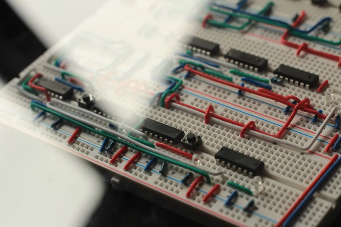 Close-up of hand-bent jumper wires, 74LS logic chips and tactile buttons on a breadboard