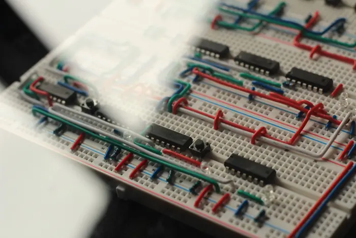 Close-up of hand-bent jumper wires, 74LS logic chips and tactile buttons on a breadboard